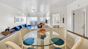 A spacious living area with a glass-top dining table surrounded by wicker chairs, a blue sofa, and a view of the outdoors. - H157: Bright Villa, Sweeping Ocean Views, Golf Cart, WIFI (Avalon)