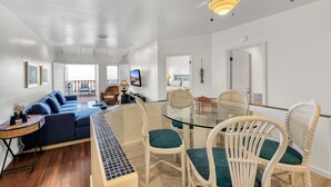 A spacious living area with a glass dining table, wicker chairs, a blue sofa, and a ceiling fan. - H157: Bright Villa, Sweeping Ocean Views, Golf Cart, WIFI (Avalon)