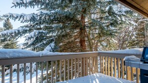 Un terrazza in legno con ringhiere imbiancate dalla neve e un barbecue.