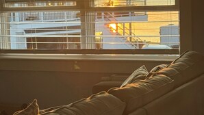 A window with horizontal blinds, a sofa with cushions, and a view of a building with a staircase.