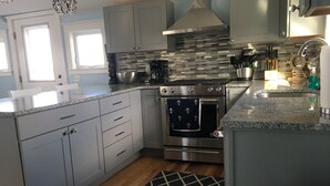 A modern kitchen with grey cabinets, a stainless steel range hood, a built-in oven, and a granite countertop.