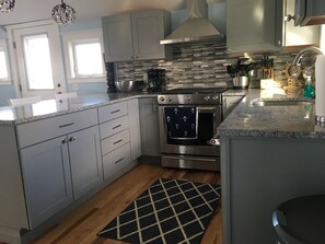 A modern kitchen with grey cabinets, a stainless steel range hood, a built-in oven, and a granite countertop. - Newly renovated Beach House - near Boston (Weymouth)