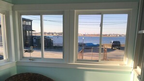 A room with a large window overlooking a body of water, a patterned chair, and a small table.