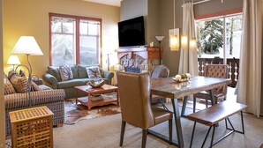 A living room with a sofa, a dining table, a television, and a fireplace. - Wanderlust Suite (with AC unit!) by Cottonwood Lodging (Solitude)
