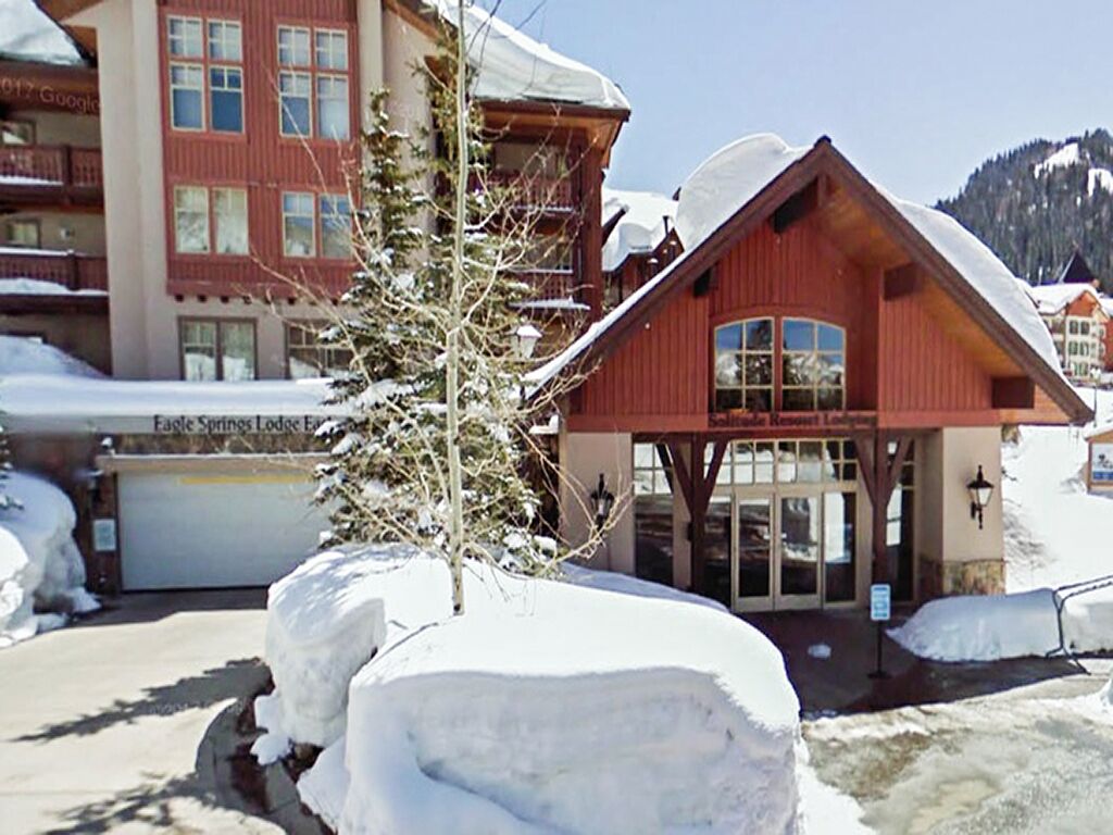 Un albergue con fachada roja y una entrada amplia. La nieve se acumula alrededor del edificio, y un árbol es visible en primer plano.