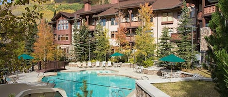 A resort with a central pool, lounge chairs, and a mountainous backdrop.