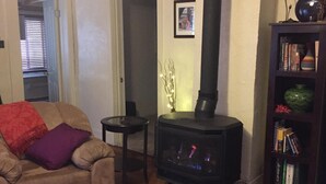 Un salon chaleureux avec un poêle à bois, un canapé, une petite table et une bibliothèque.