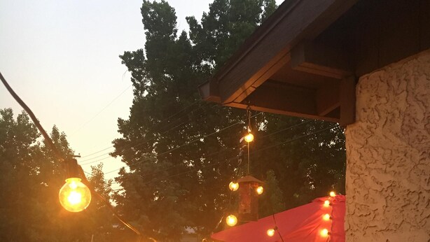 Un espace extérieur aménagé en terrasse, avec des guirlandes lumineuses, un parasol rouge et un mur en briques.
