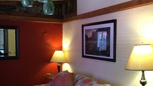 Une chambre à coucher avec un lit, deux lampes, un tableau encadré et une petite table sur laquelle se trouve une télécommande.