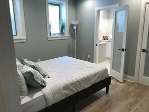 A bedroom with a bed, a bedside lamp, a window, and a door leading to a bathroom. - Luxury Condo 2br close to Metro & NIH Walter Rees/Sightseeing/Museums/Zoo/shops (Chevy Chase)