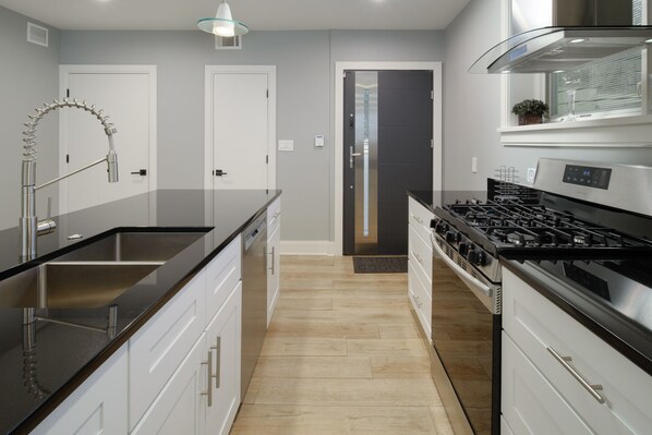 A modern kitchen with a stainless steel range hood, a black countertop, and white cabinetry. - Luxury Condo 2br close to Metro & NIH Walter Rees/Sightseeing/Museums/Zoo/shops (Chevy Chase)