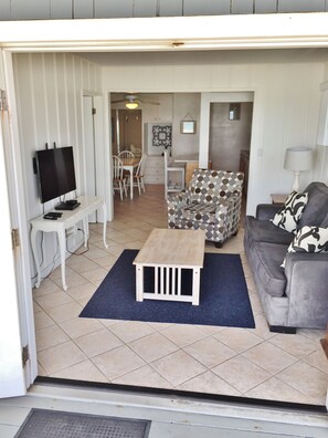 A living room with a TV, a patterned armchair, a sofa, and a small wooden table. - Oceanfront - Private Beach! (Oceanside)