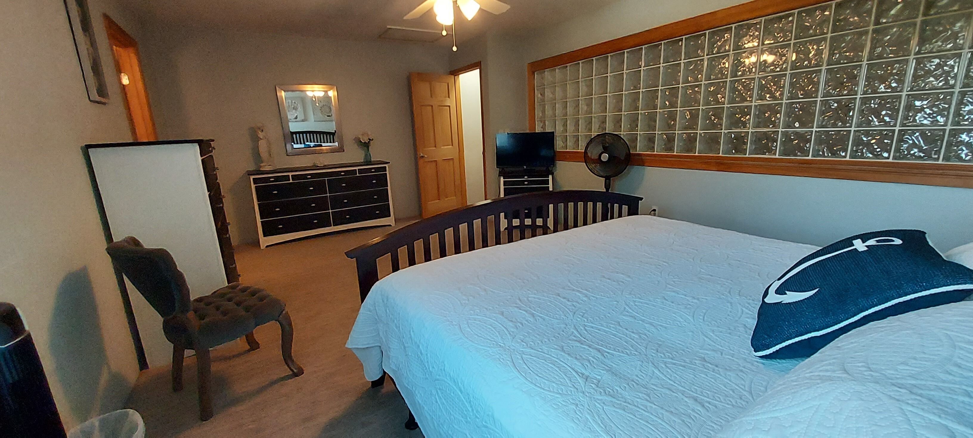 Une chambre à coucher comprenant un lit, une commode, une chaise et un téléviseur.