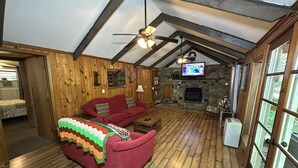 Una habitación acogedora con un sofá rojo, una chimenea de piedra, vigas de madera y un televisor.