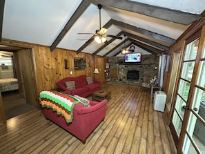 A cozy room with a red sofa, a stone fireplace, wooden beams, and a television.