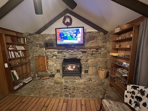 A cozy living room with a stone fireplace, a television mounted above it, and wooden bookshelves on either side.