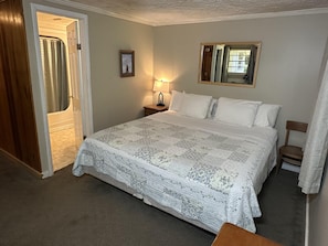 A bedroom with a bed, a nightstand, a lamp, a framed picture, and a window.