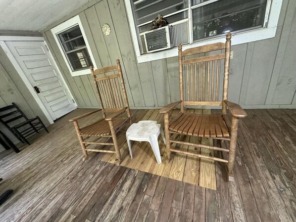 Two wooden chairs with a small table in a room with wooden floors and a window with air conditioning units.