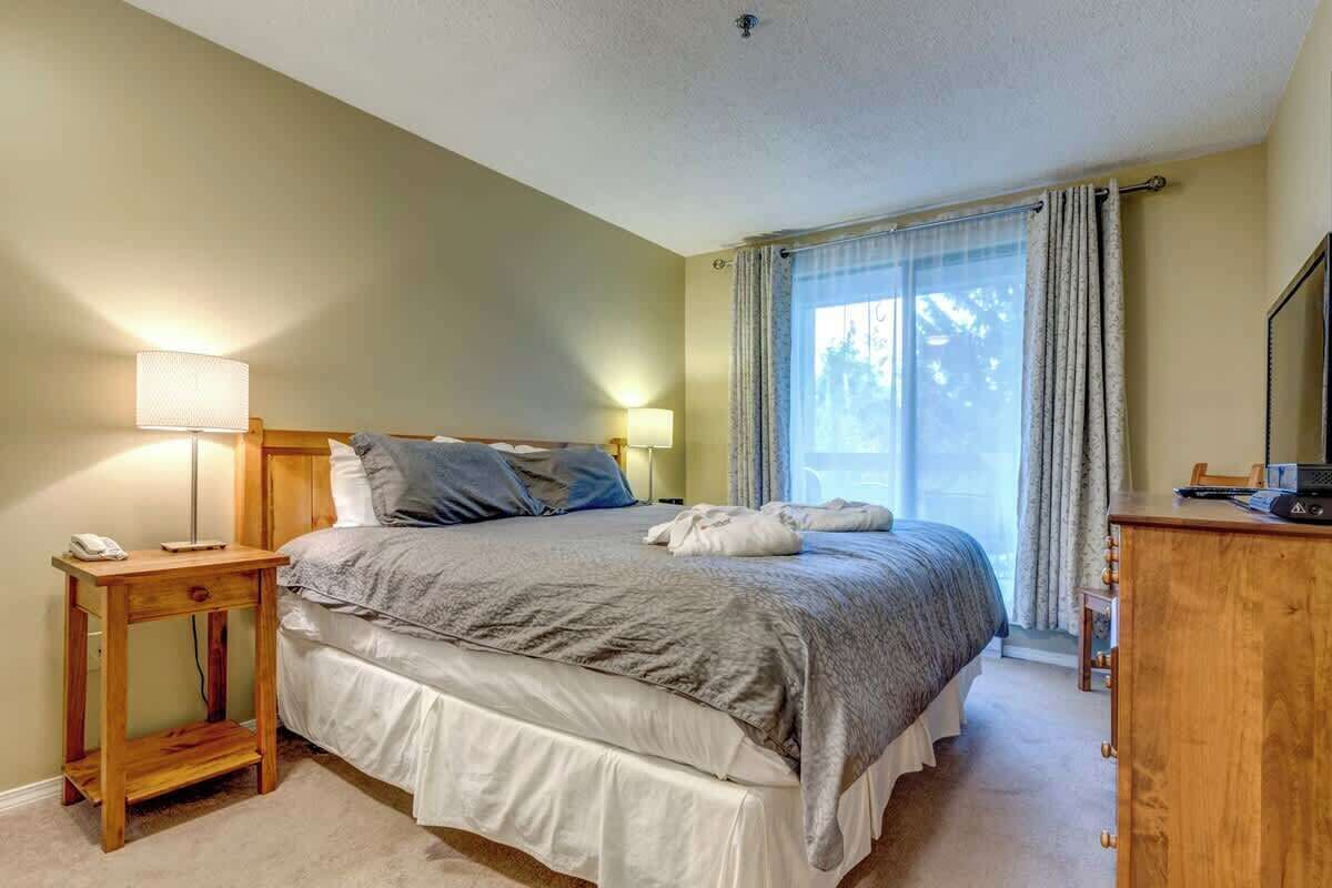 Ett sovrum med en säng, sängbord, en lampa, en byrå och ett fönster med gardiner.
