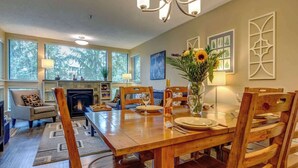 A dining room with a wooden table, chairs, a vase with flowers, and a fireplace. - Greystone Lodge 210 Ski-in/Out by Acer Vacations (Whistler)