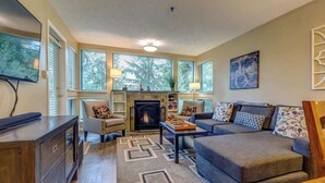 A living room with a fireplace, sofa, armchair, and a flat-screen TV. - Greystone Lodge 210 Ski-in/Out by Acer Vacations (Whistler)