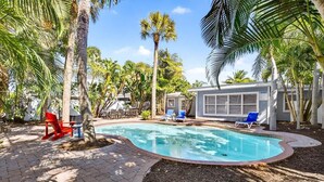 A swimming pool with lounge chairs, palm trees, and a small building with a window. - Lantana Cabana 3BR North Clearwater Beach Home (Cleawater)