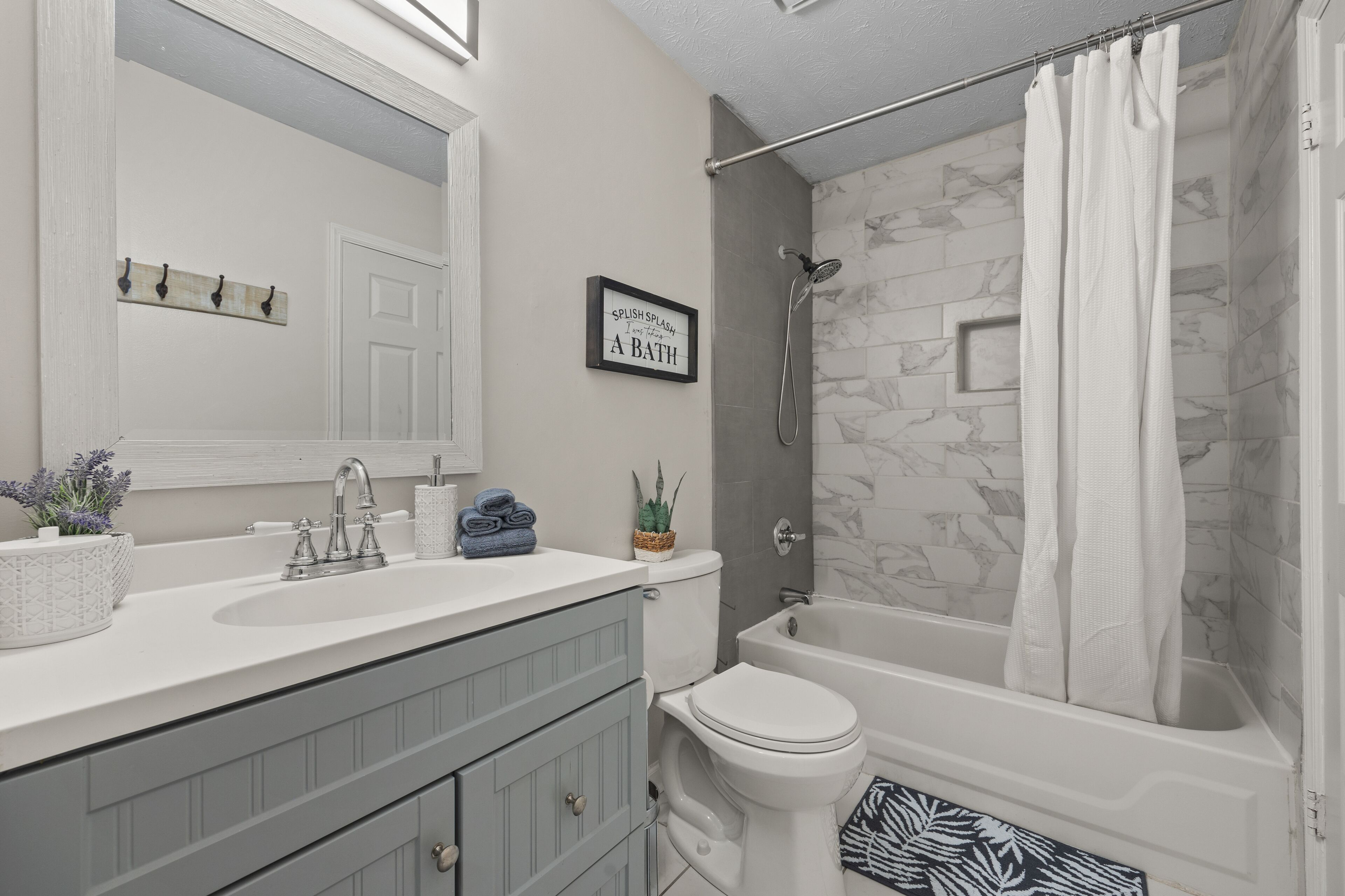A bathroom with a white sink, a toilet, and a bathtub. There is a shower curtain, a towel rack, and a framed quote on the wall.