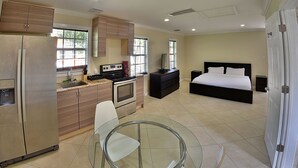 Une chambre d’hôtel moderne équipée d’une cuisine, d’une table à manger en verre, d’un lit et d’un téléviseur.