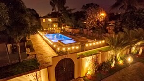 Une piscine bien éclairée, dotée d’un espace patio et entourée d’arbres et d’une maison.