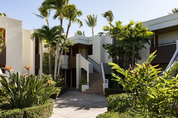 A modern building with a central staircase, surrounded by lush greenery and palm trees.