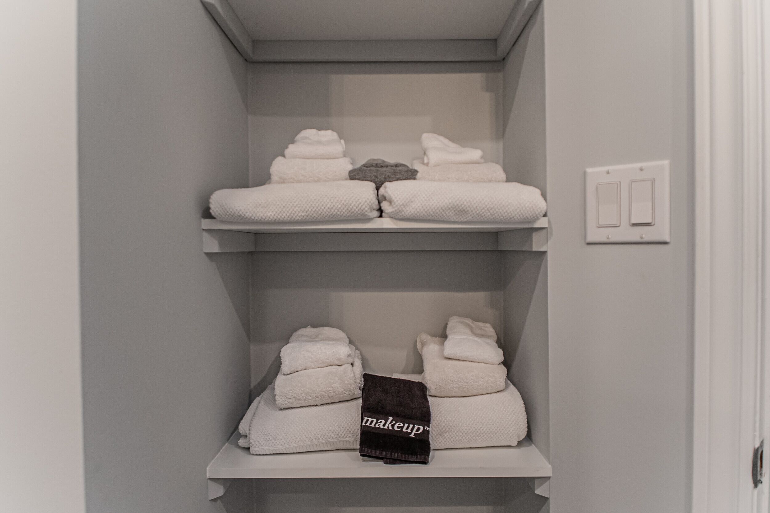 Un baño con dos repisas que sostienen toallas dobladas y una toalla para maquillaje.
