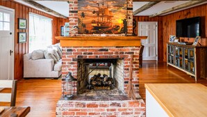 Una sala de estar con chimenea de ladrillo, vigas de madera, un sofá y un televisor.