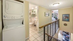 A laundry room with a washer and dryer, a staircase leading to a second floor, and a view of a living area with a fireplace.