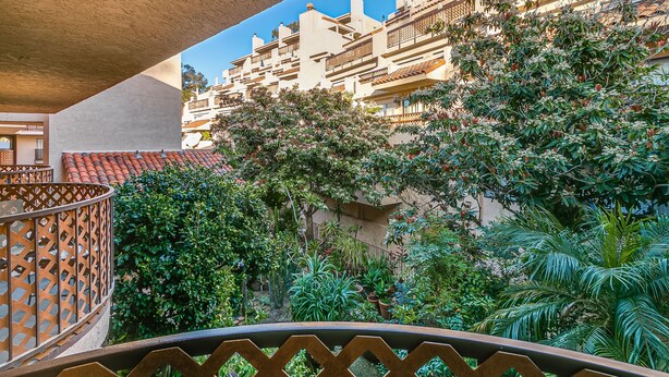 A courtyard with a view of a building with balconies and a variety of plants.