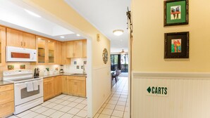 A kitchen with wooden cabinets, a white stove, and a microwave. There are framed pictures on the wall and a sign indicating 'CARTS'.