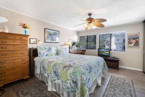 A bedroom with a bed, dresser, ceiling fan, and artwork on the walls.
