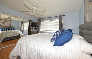 Une chambre avec un grand lit, un ventilateur de plafond et une fenêtre avec des stores.
