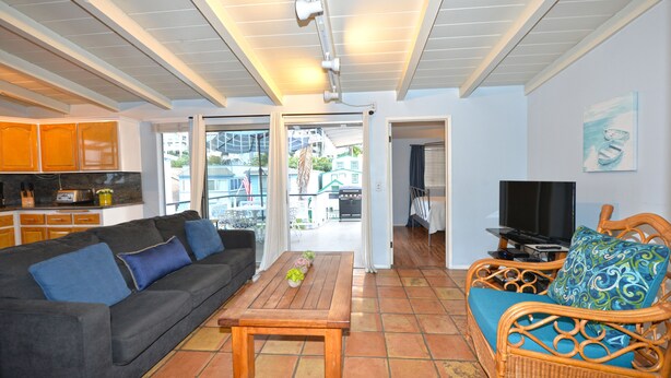 A living room with a sofa, a coffee table, a wicker chair, and a television. - 211CLU: Home with Deck, Golf Cart, 1 Block to the Beach, Pet Friendly, WIFI - 21 (Avalon)