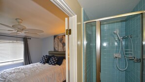 A bedroom with a bed, a ceiling fan, a shower with a glass door, and a window with blinds. - 211CLU: Home with Deck, Golf Cart, 1 Block to the Beach, Pet Friendly, WIFI - 21 (Avalon)