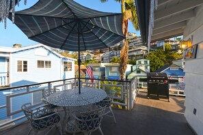 Un balcon avec une table ronde et des chaises, un barbecue et une vue sur un quartier situé sur la côte.