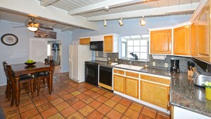 A kitchen with wooden cabinets, a dining table with chairs, a ceiling fan, and a tiled floor. - 211CLU: Home with Deck, Golf Cart, 1 Block to the Beach, Pet Friendly, WIFI - 21 (Avalon)