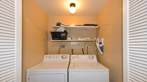 A laundry room with two white washers and dryers, a shelf with various items, and a wall-mounted phone. - 211CLU: Home with Deck, Golf Cart, 1 Block to the Beach, Pet Friendly, WIFI - 21 (Avalon)
