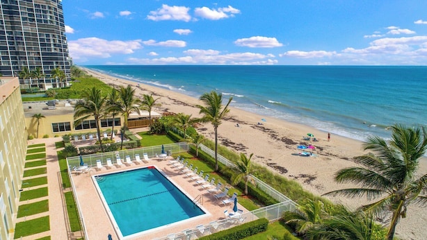 A hotel with a pool, beach view, and palm trees.