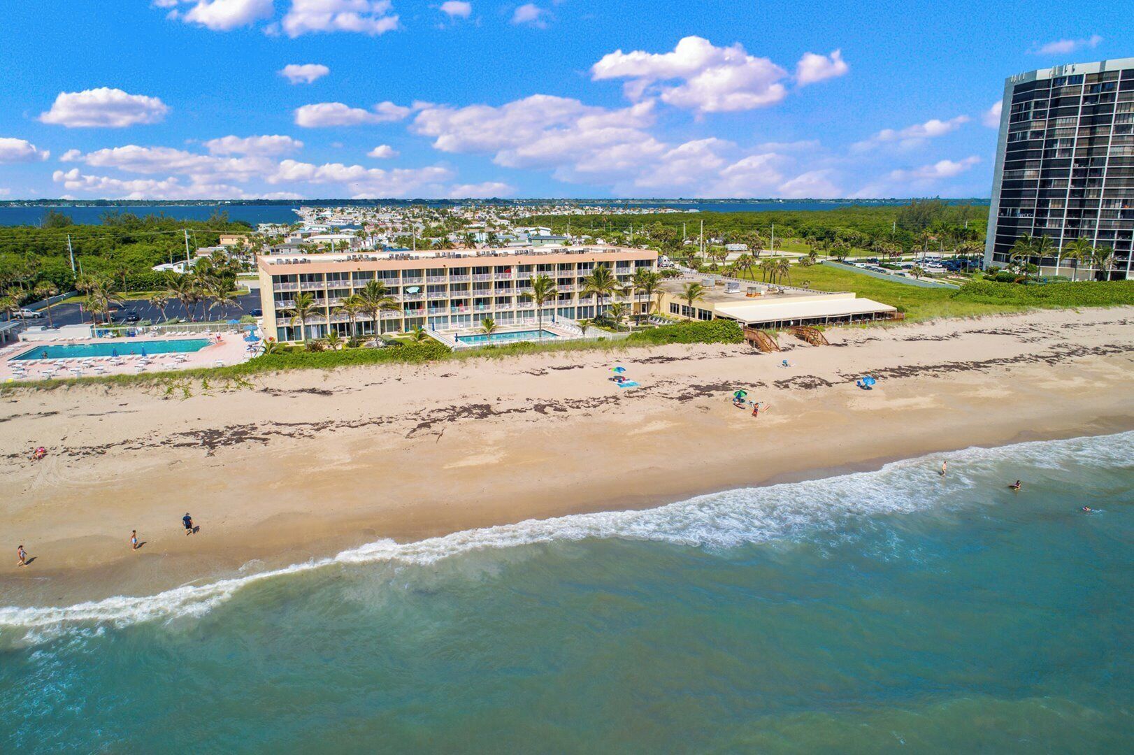 Un hotel frente a la playa con varios balcones, piscina y acceso directo a la playa.