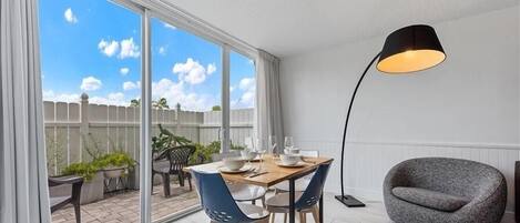 A modern living room with a dining area, large windows, and a grey armchair.