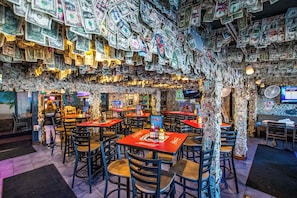 A restaurant with tables covered in dollar bills, a TV screen, and a menu board.