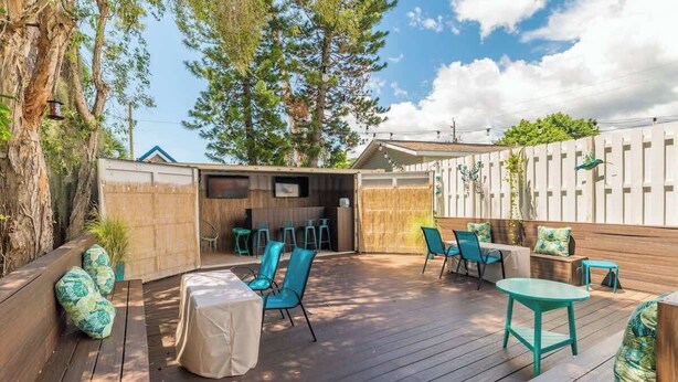 An outdoor patio with wooden decking, blue chairs, and a covered table.
