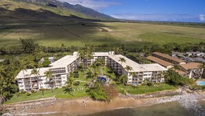 Um resort com vários edifícios, uma praia e montanhas ao fundo.
