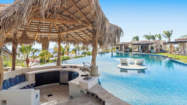 A resort pool area with a thatched-roof gazebo, a curved pool, and a stone-tiled deck.