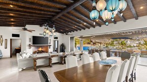 A spacious living area with a fireplace, a dining table with chairs, and a view of an outdoor pool area.